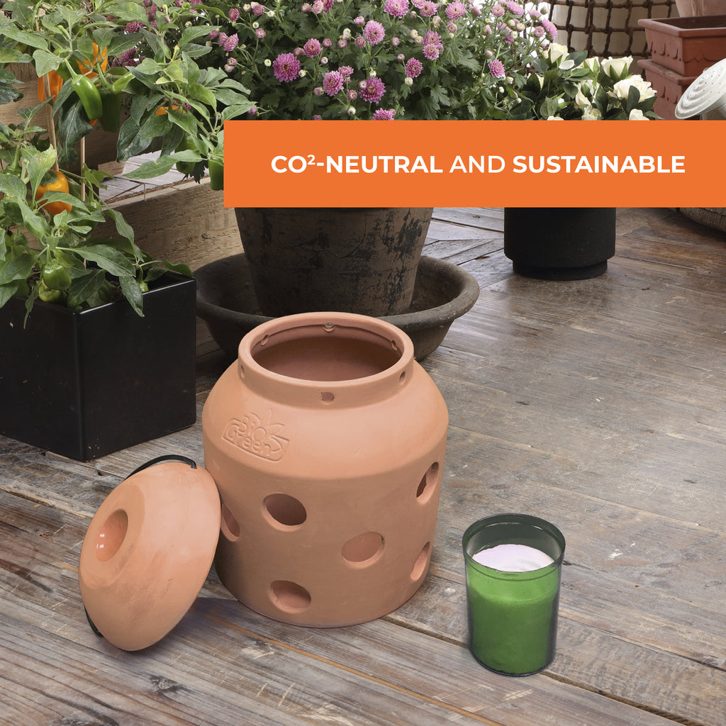 This image shows the Biogreen Firefly Frost Guard Heater placed beside a plant pot, with a label highlighting that it is CO₂-neutral and sustainable. The eco-friendly design is powered by biomass candles, ensuring efficient, non-electric heating for plant protection during colder months. The image features the heater's terracotta design, with a lid and holes for optimal heat distribution, as well as a green candle placed next to it, emphasizing sustainability.
